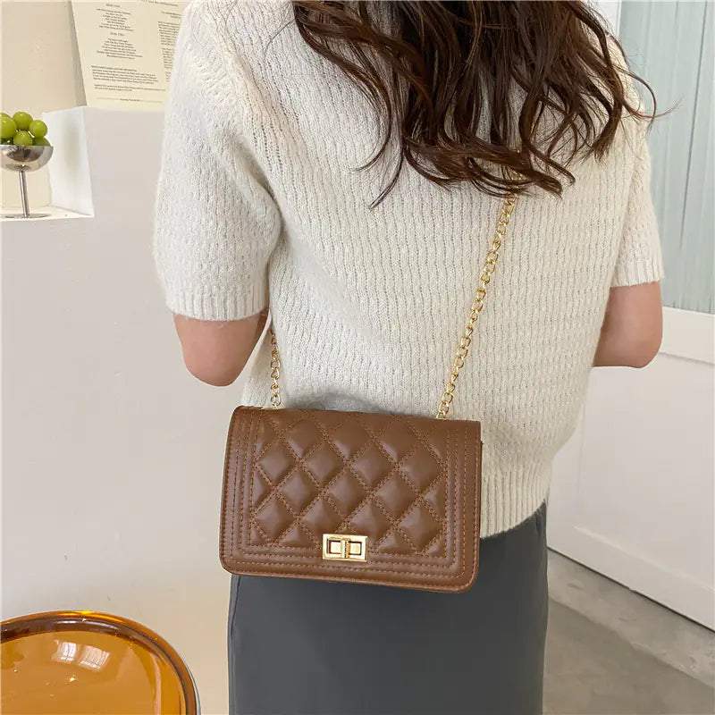 Person wearing a beige sweater and holding a brown quilted handbag with a gold chain.