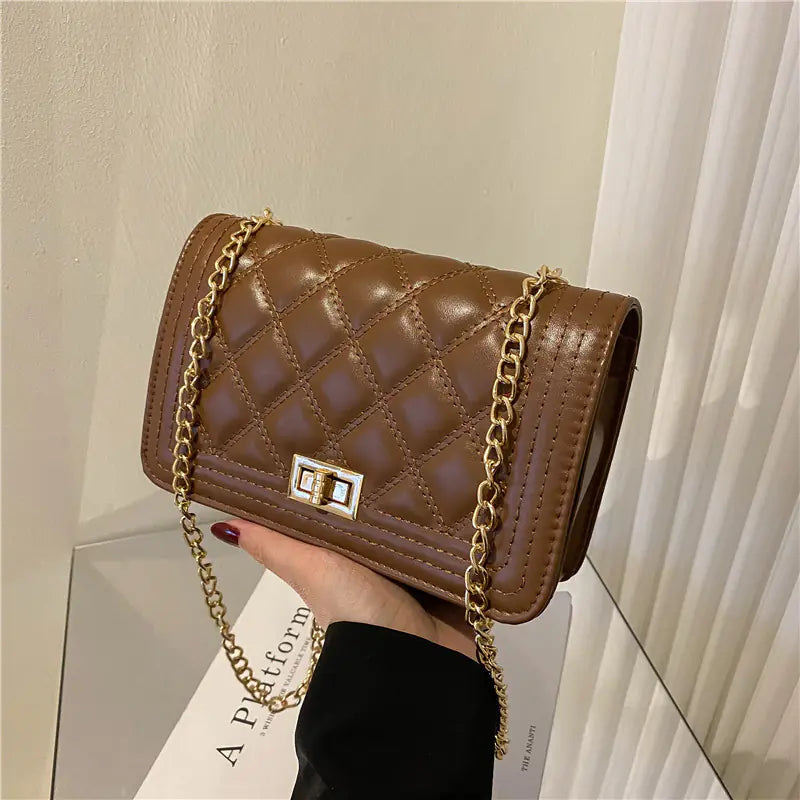 Brown quilted handbag with gold chain held by a hand on a neutral background