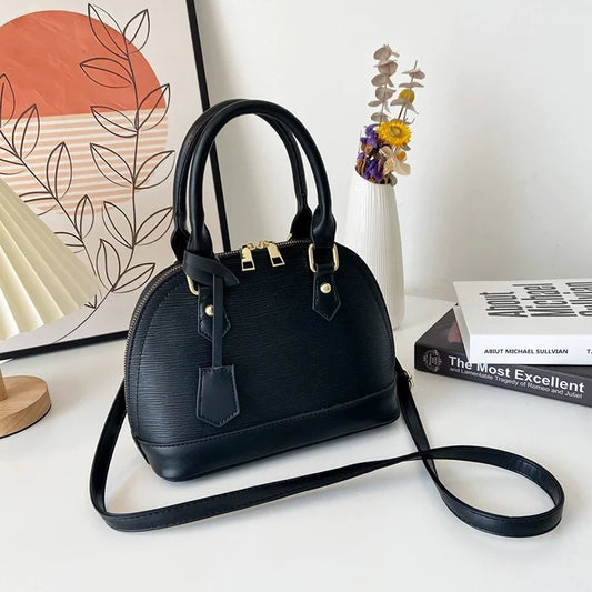 Black handbag on a white surface with a decorative vase and books in the background