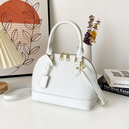 White handbag with gold accents on a surface with books and decorative items in the background